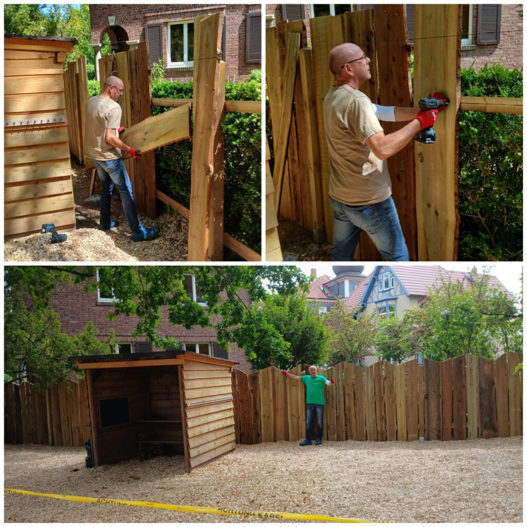 Mann Baut einen Zaun aus großen Holzbrettern und schaut zufrieden.