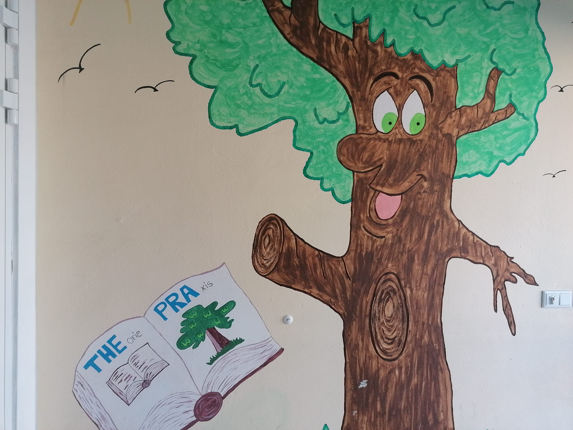 Wandgemälde eines Baums mit Augen, Nase und Mund. Dieser hat vor sich ein Buch aufgeschlagen in dem THEPRA steht.