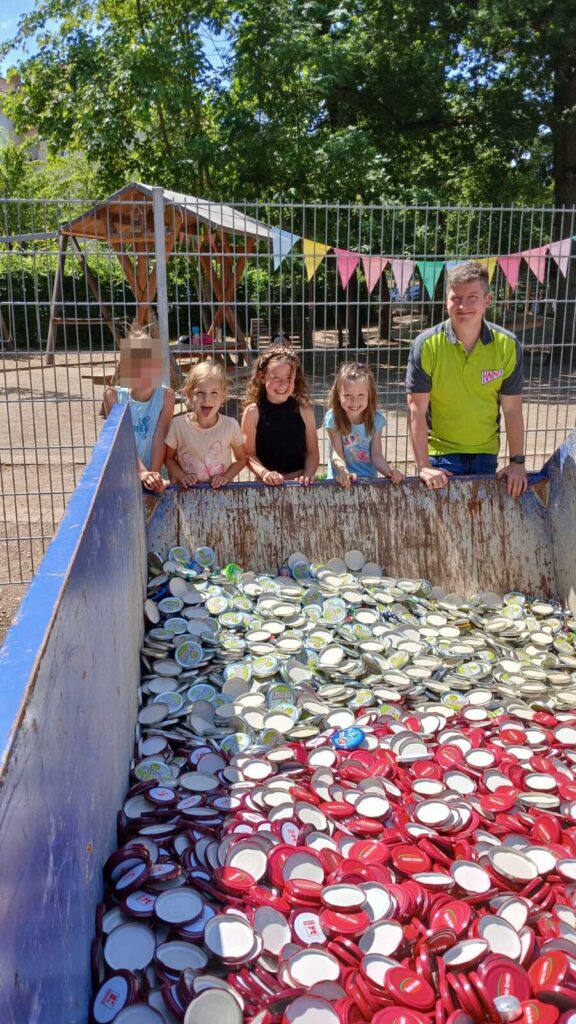 Kinder schauen lachend auf Container voll mit Korken und Deckeln.