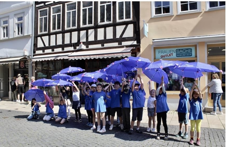 Kinder mit blauen THEPRA T-Shirt und Regenschirm freuen sich.