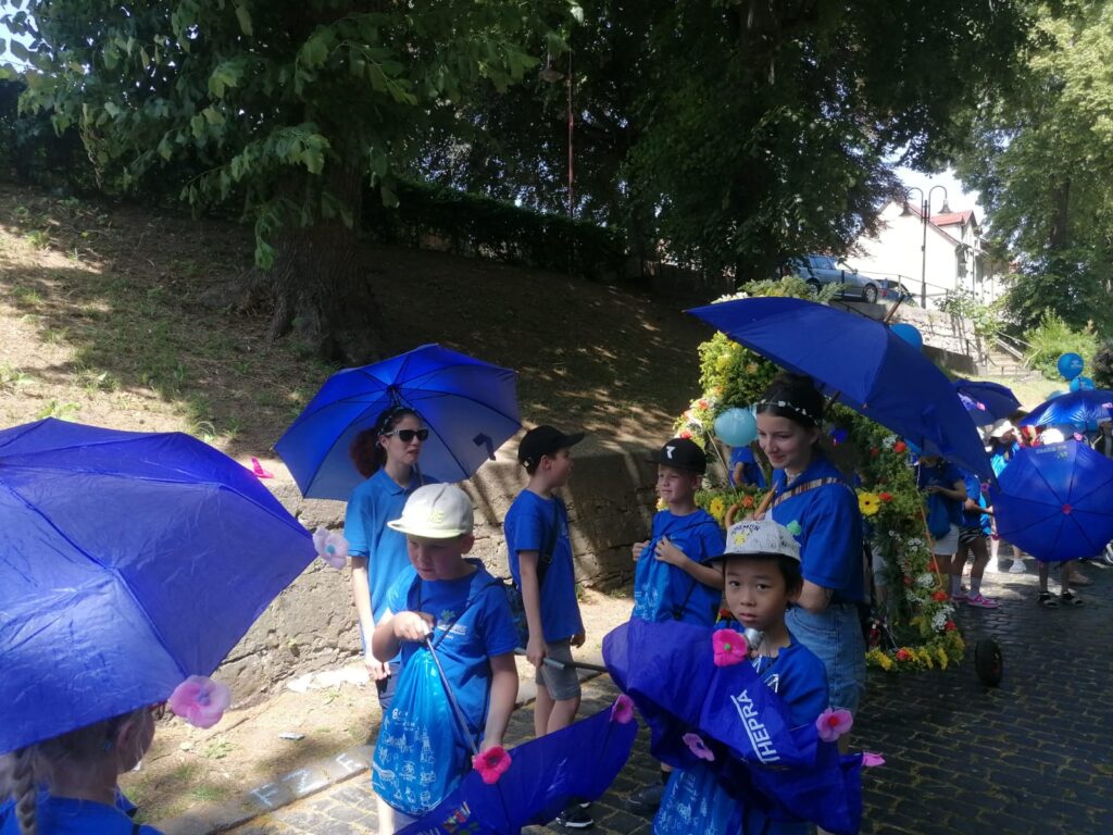 Kinder und Erzieherin mit blauen THEPRA T-Shirts und Sonnenschirmen beim Stadtfest in Bad Langensalza.