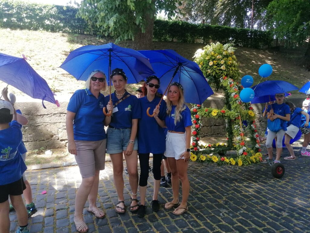 Vier Erzieherinnen mit blauen THEPRA T-Shirt und Regenschirm auf dem Stadtfest.