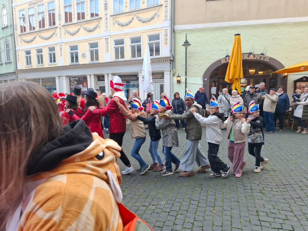 Kinder machen mit Faschingshüten eine Polonaise durch die Stadt.