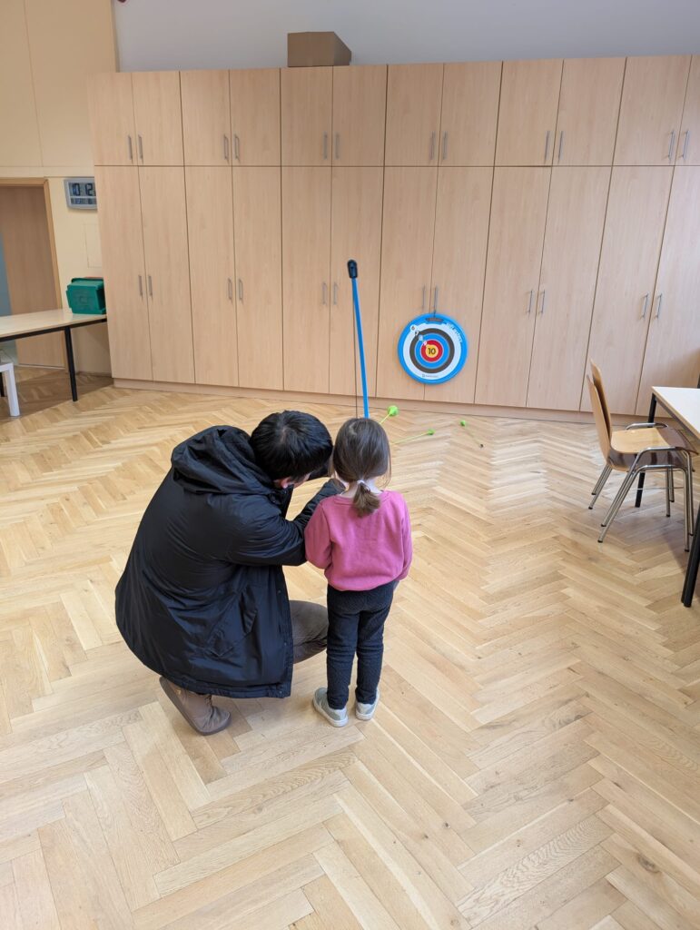 Frau Hilft einem Mädchen mit einem Spielzeugbogen zu schießen.